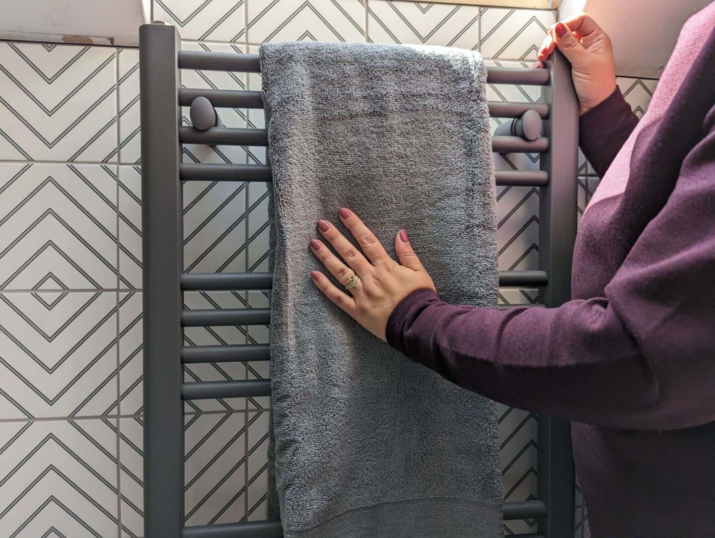 Woman strokes a grey bath towel hanging on a matt grey towel radiator