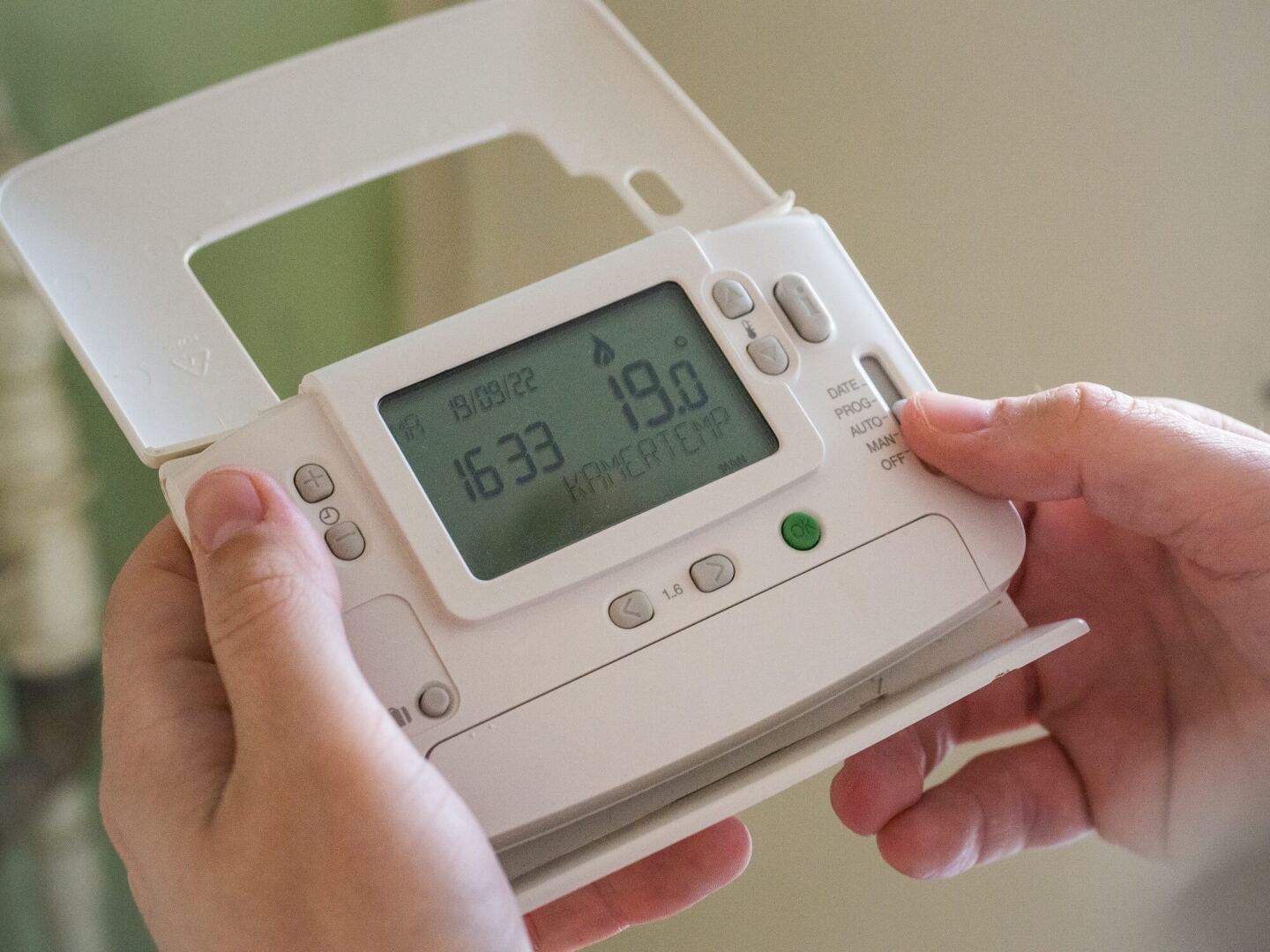 A mans hands holding a thermostat for controlling the heating system and helping to reduce heating bills