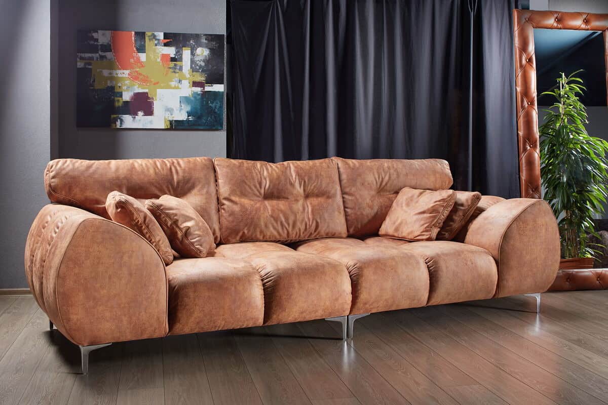 How to choose the perfect sofa for your lifestyle. Brown suede sofa on wooden floor with artwork behind and mirror to the right.