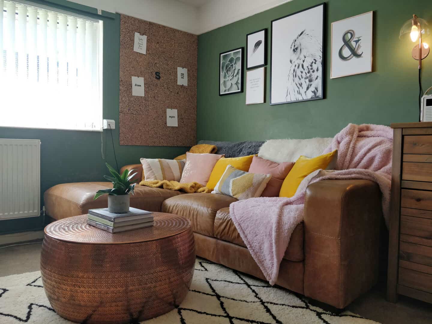 Autumn home updates with Habitat. A green living room featuring a brown leather sofa, copper coffee table and pink and yellow velvet cushions.