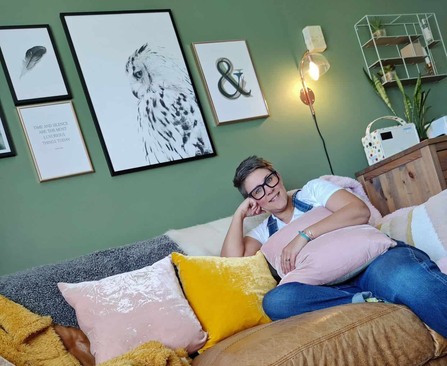 Autumn home updates with Habitat. Blogger Stacey Sheppard in her green living room sat in her brown leather sofa amongst pink and yellow velvet cushions.