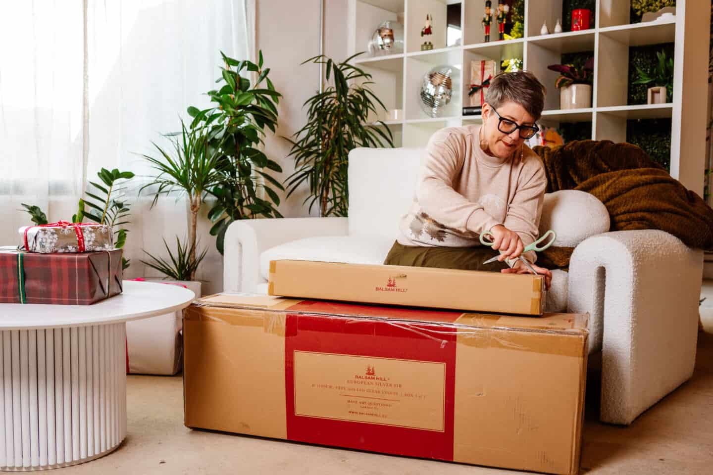 A woman in her forties sat on a sofa unpacking realistic Christmas decorations from Balsam Hill