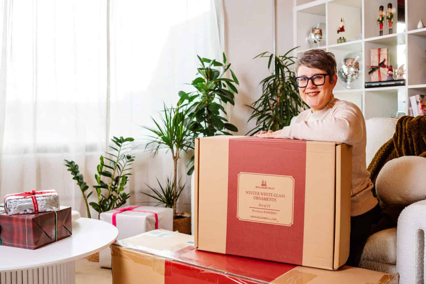 A woman in her forties sat on a sofa getting ready to unpack realistic Christmas decorations from Balsam Hill