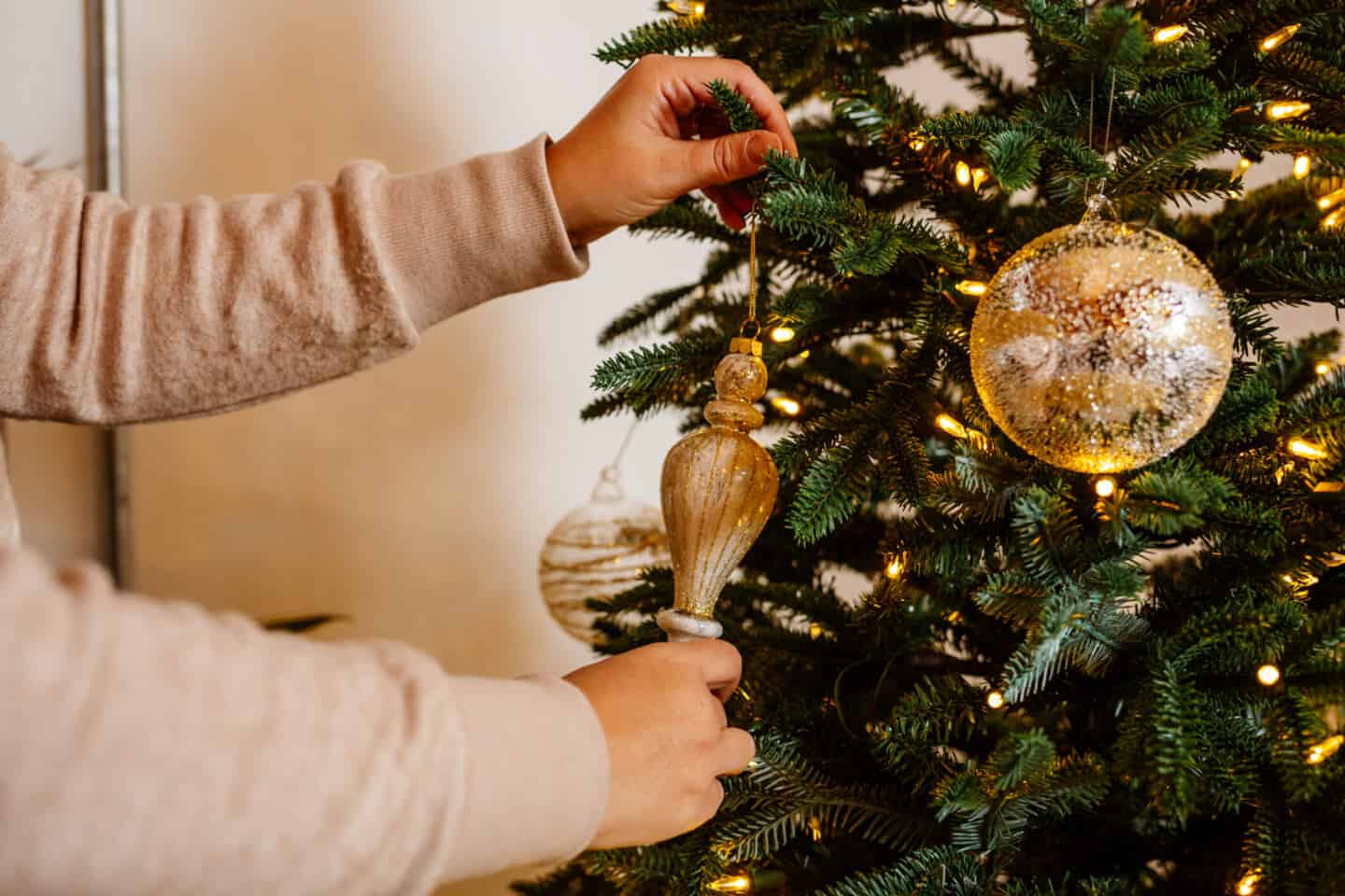 A woman in her forties hangs Christmas baubles on a realistic artificial Christmas tree from Balsam Hill