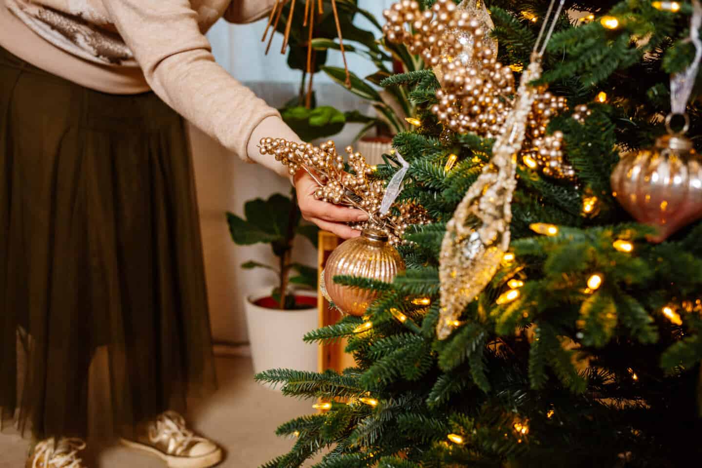 A woman in her forties sticks Christmas tree picks into a realistic artificial Christmas tree from Balsam Hill