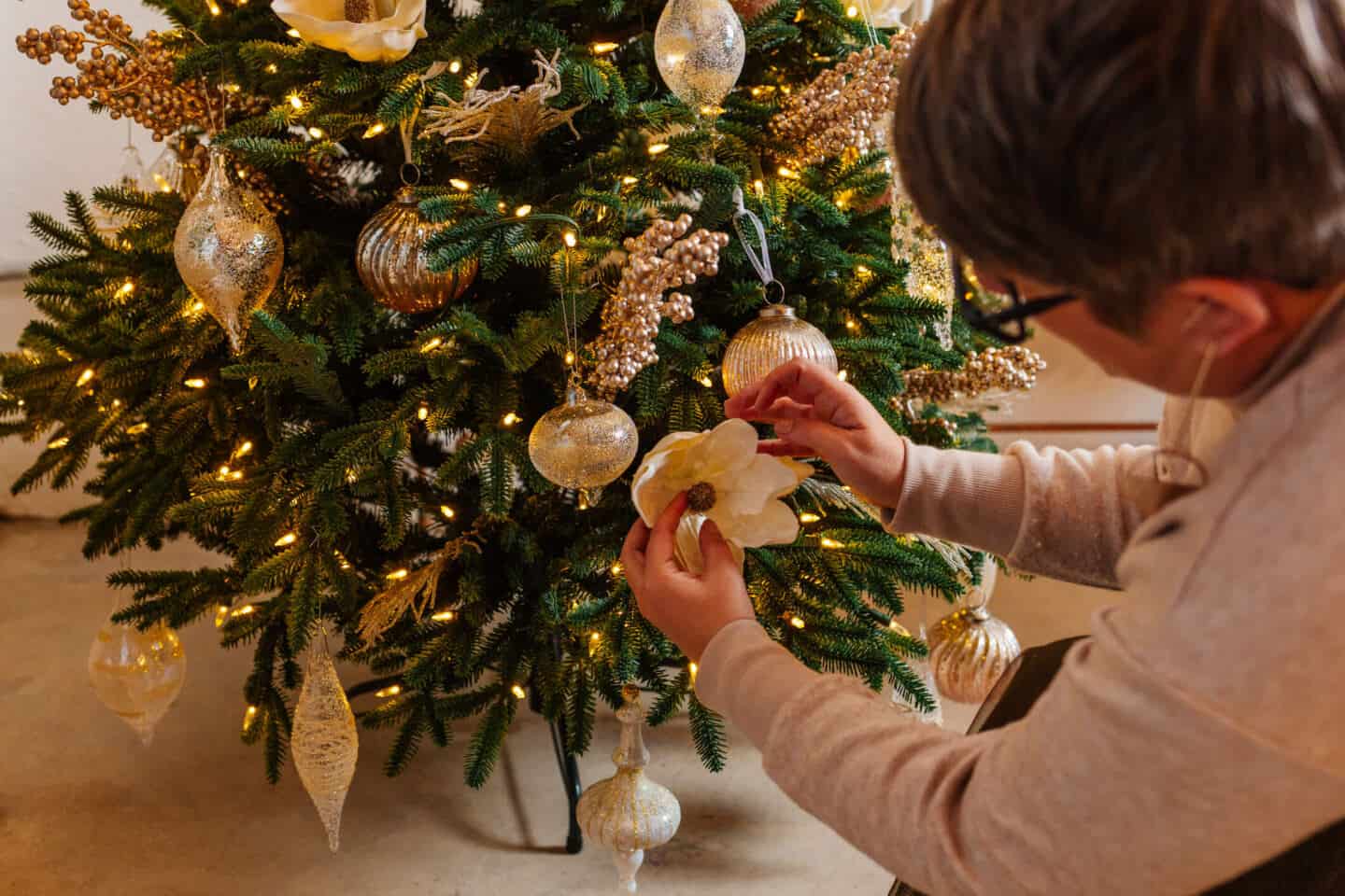 A woman in her forties sticks Christmas tree picks into a realistic artificial Christmas tree from Balsam Hill