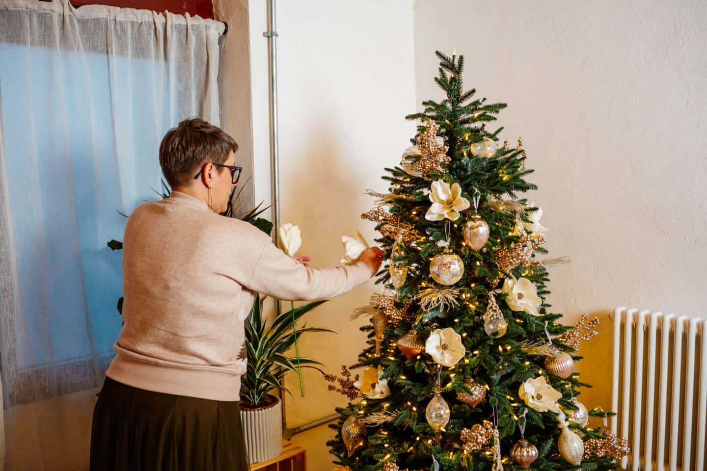 A woman in her forties sticks Christmas tree picks into a realistic artificial Christmas tree from Balsam Hill
