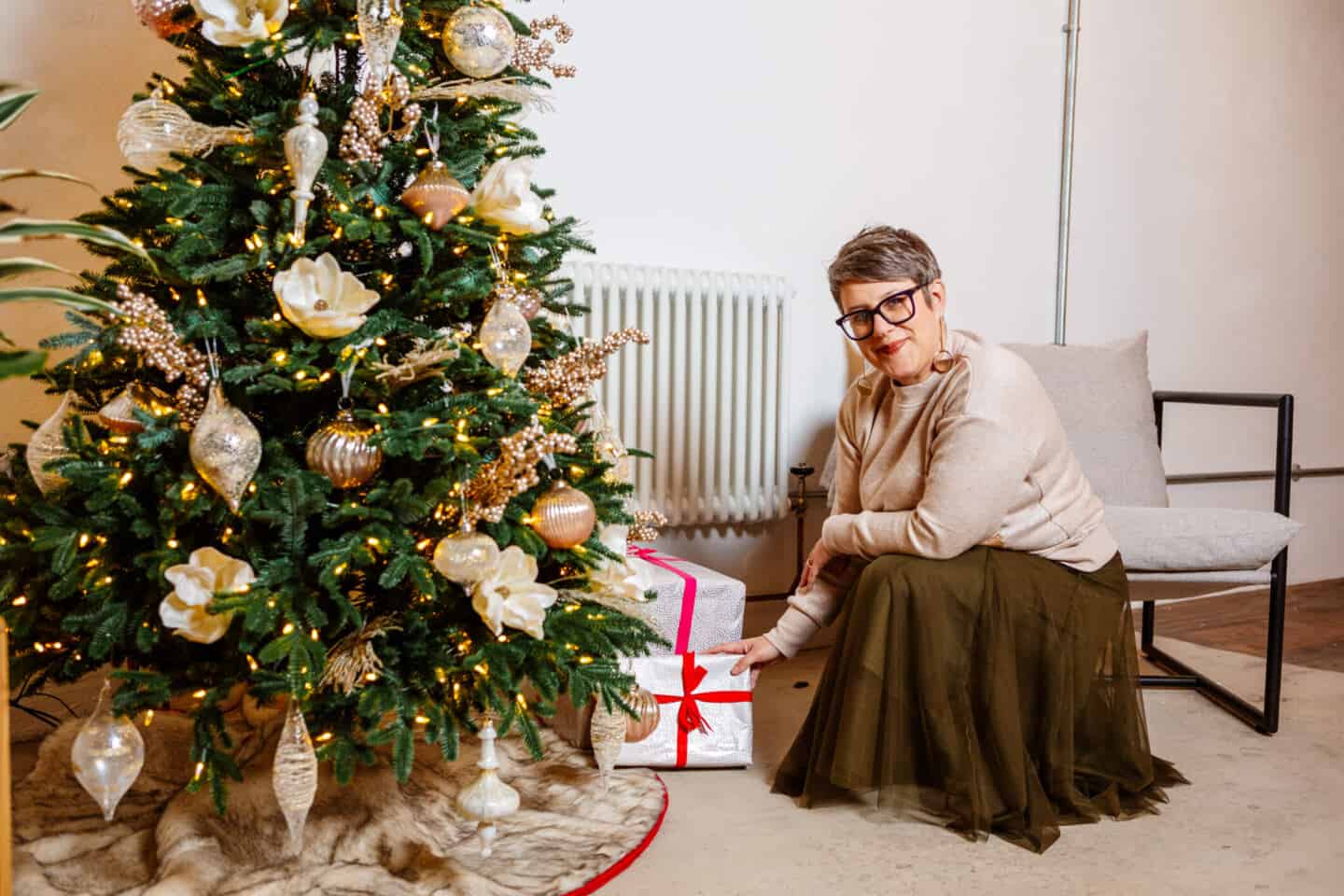 A woman in her forties places Christmas presents beneath a realistic artificial Christmas tree from Balsam Hill