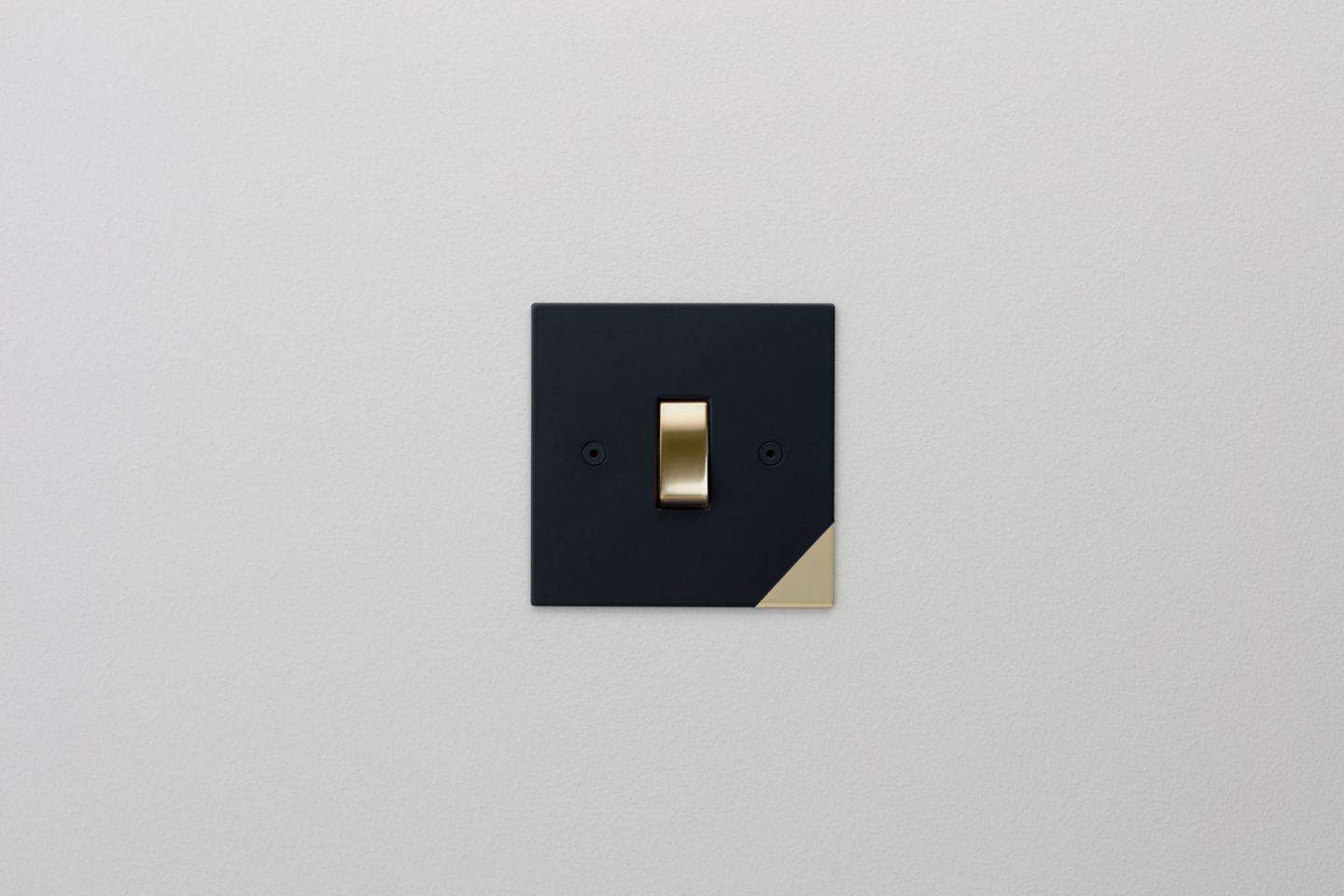 Matt black designer light switch with gold details on the wall