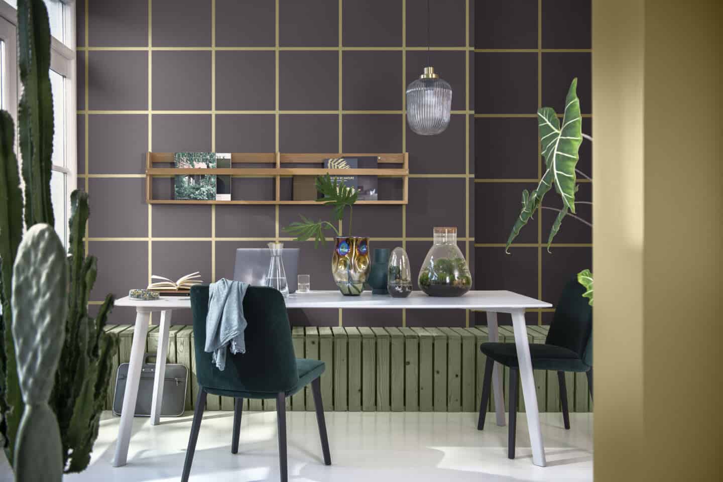 Terrariums sit on a table surrounded by plants. The wall behind is painted with checks