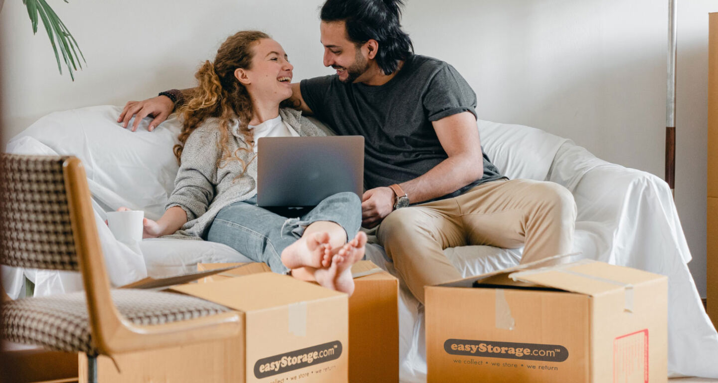 A couple sitting on a sofa surrounded by moving boxes
