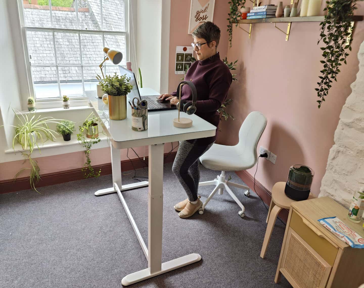 a middle aged woman stood at a standing desk in a pink office