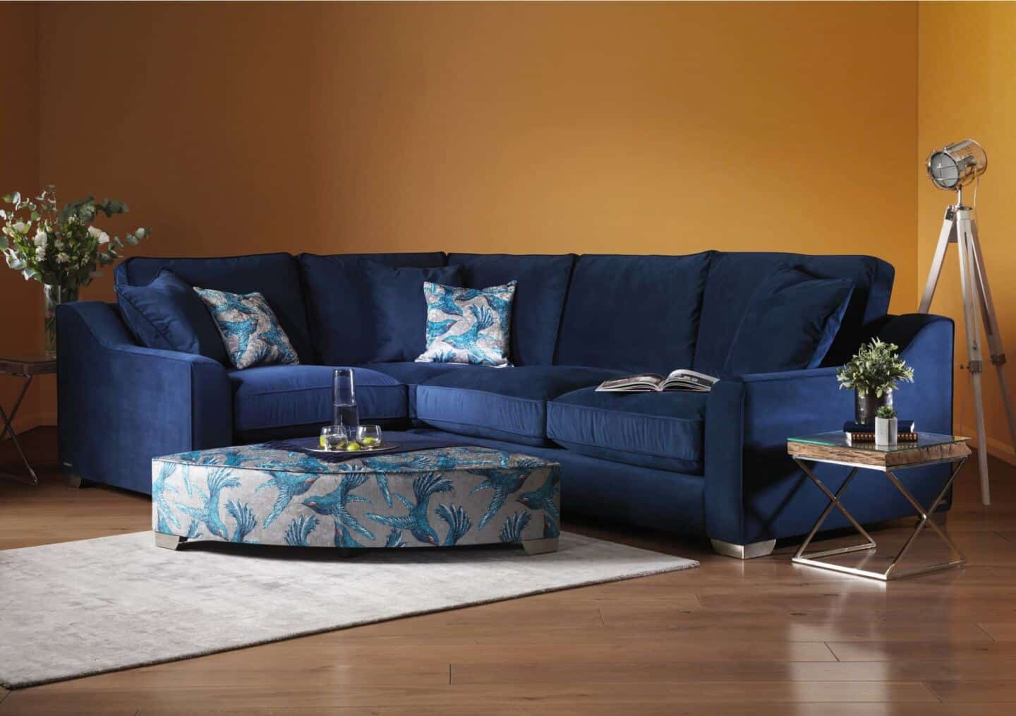 A blue sectional sofa with orange walls behind and a triangular footstool in front