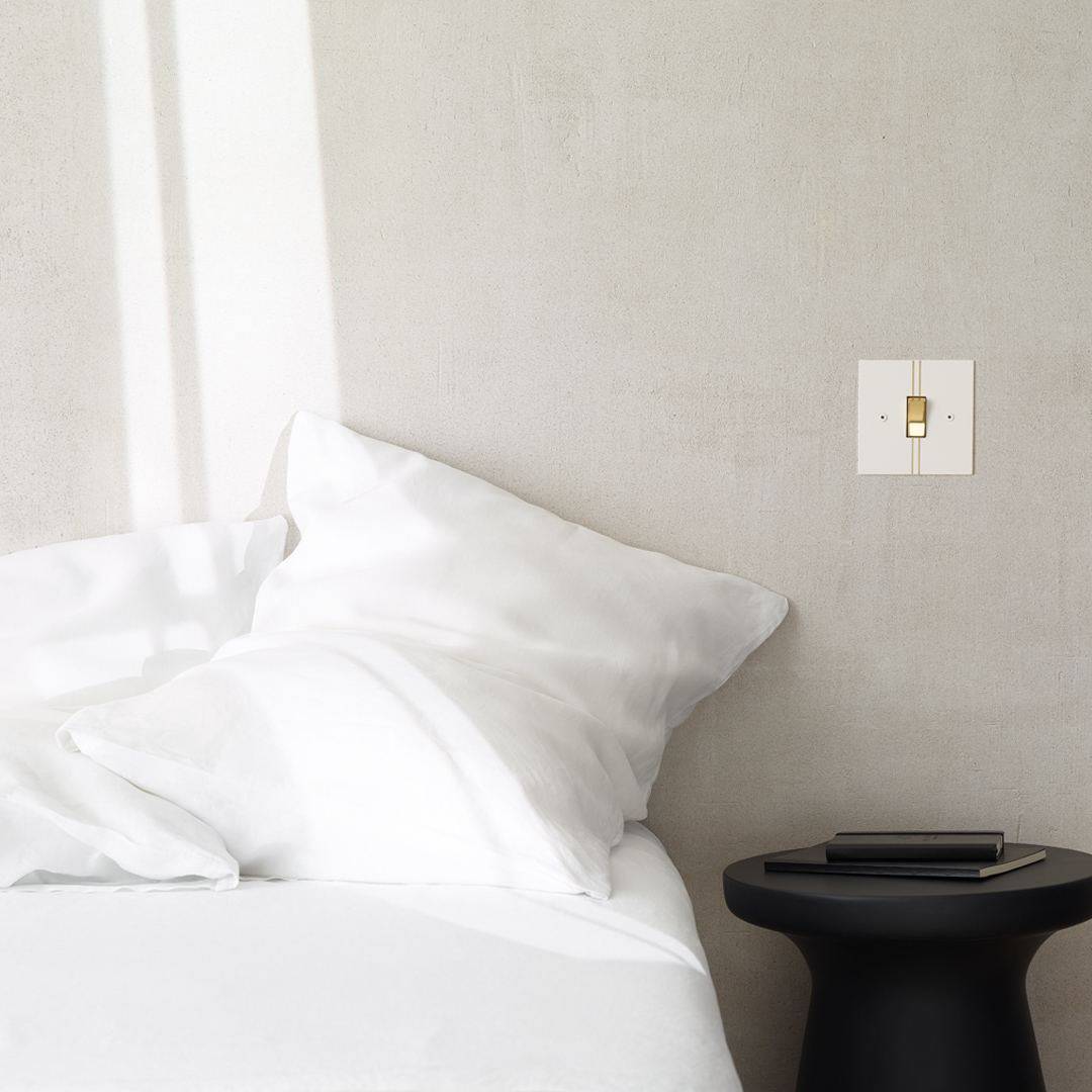 A white and gold pinstripe light switch on the wall next to a bed above a bedside table