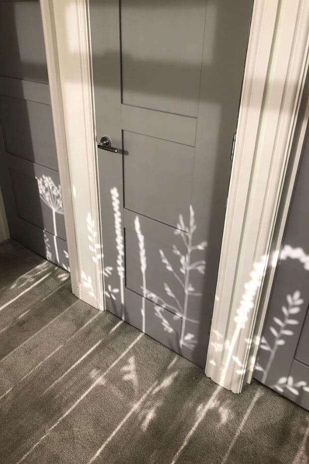 shadows cast across the floor and wall of meadow flowers created by the sunlight coming through the window film