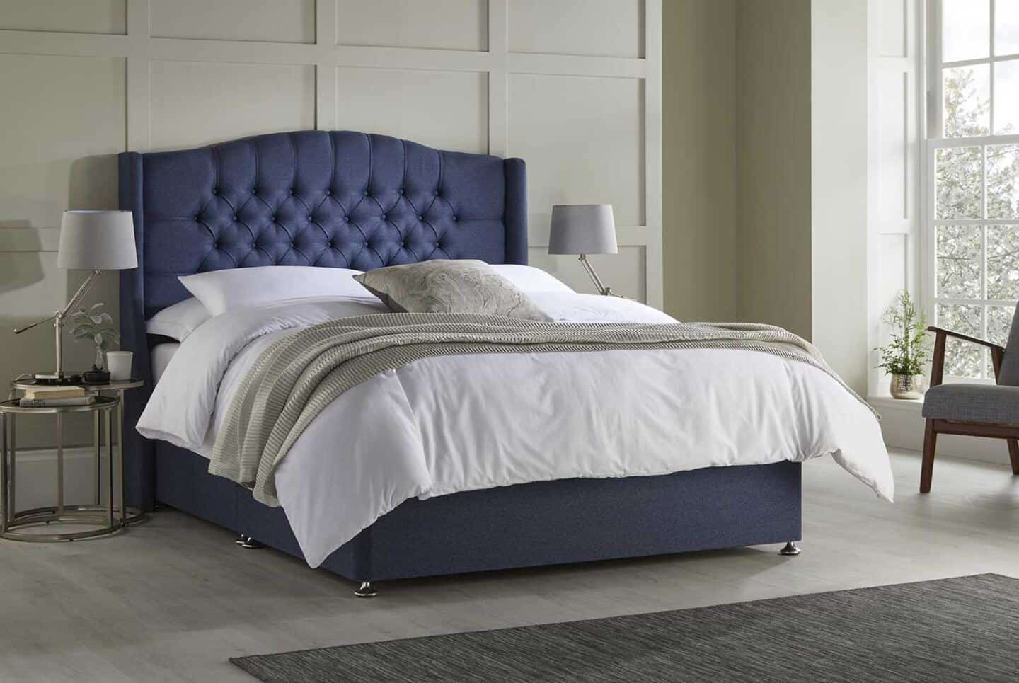 A blue upholstered ottoman bed against a sage green panelled wall