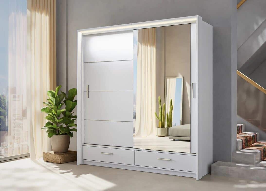 A white double wardrobe with one mirrored door and two drawers in the base. A concrete staircase runs behind and a floor to ceiling window is adjacent.