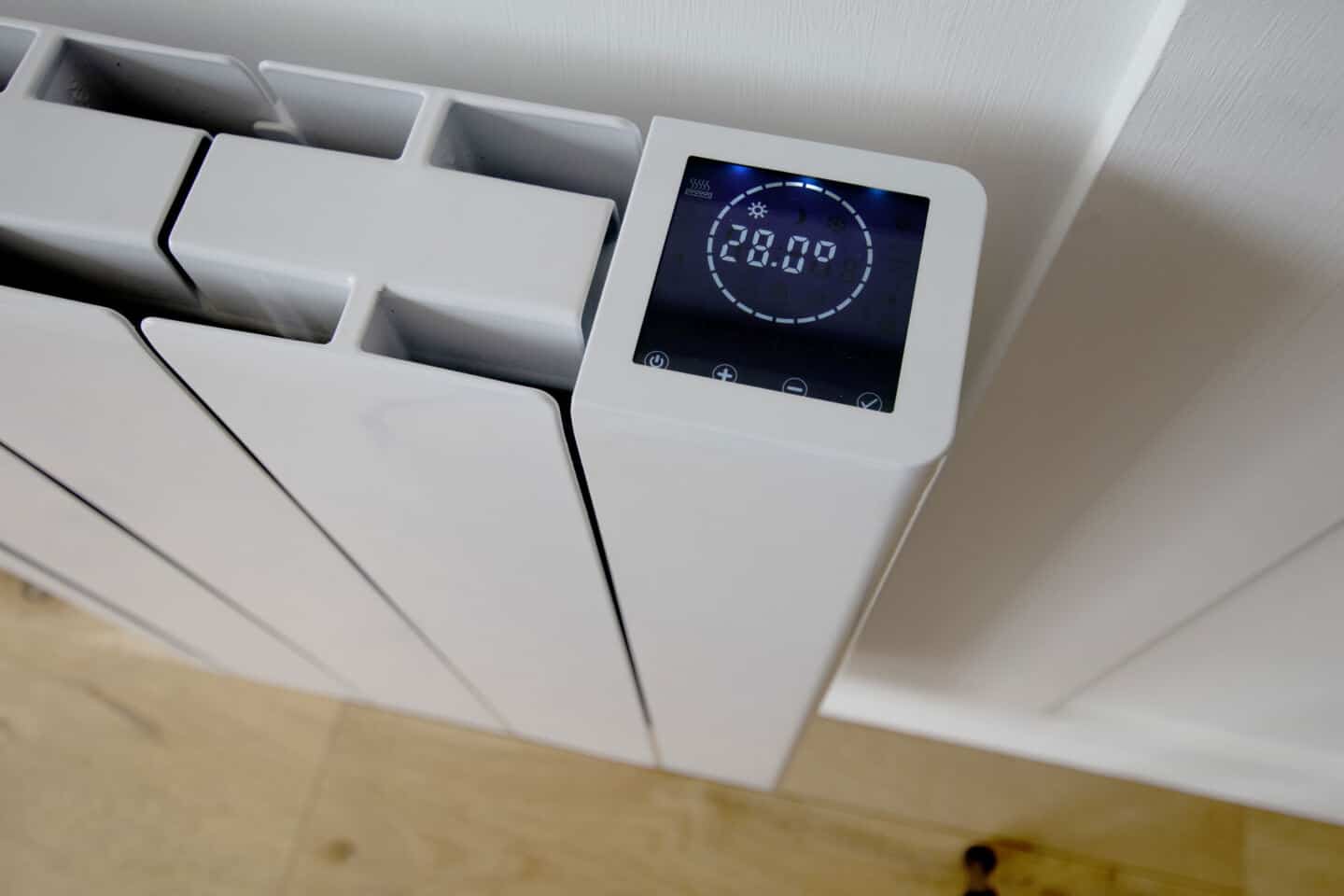 The digital display of the Ecostrad iQ Ceramic smart electric radiator mounted on a white wall.
