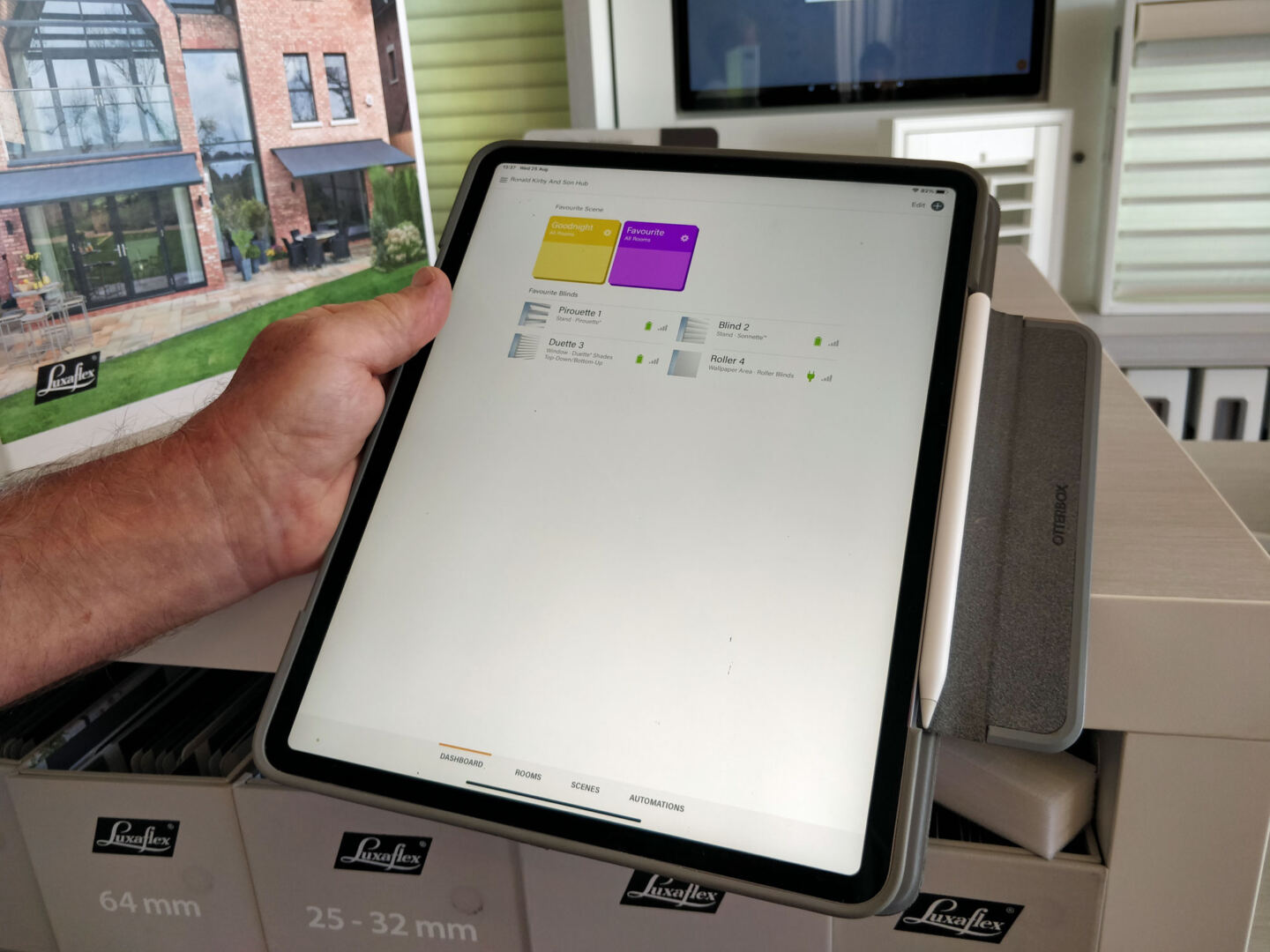 Hand holding a tablet displaying the Luxaflex blinds powerview app