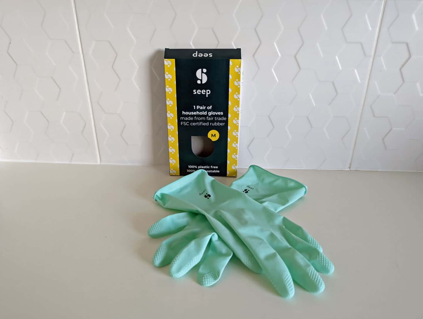 A pair of natural rubber gloves from Seep on a white worktop with white tiles behind