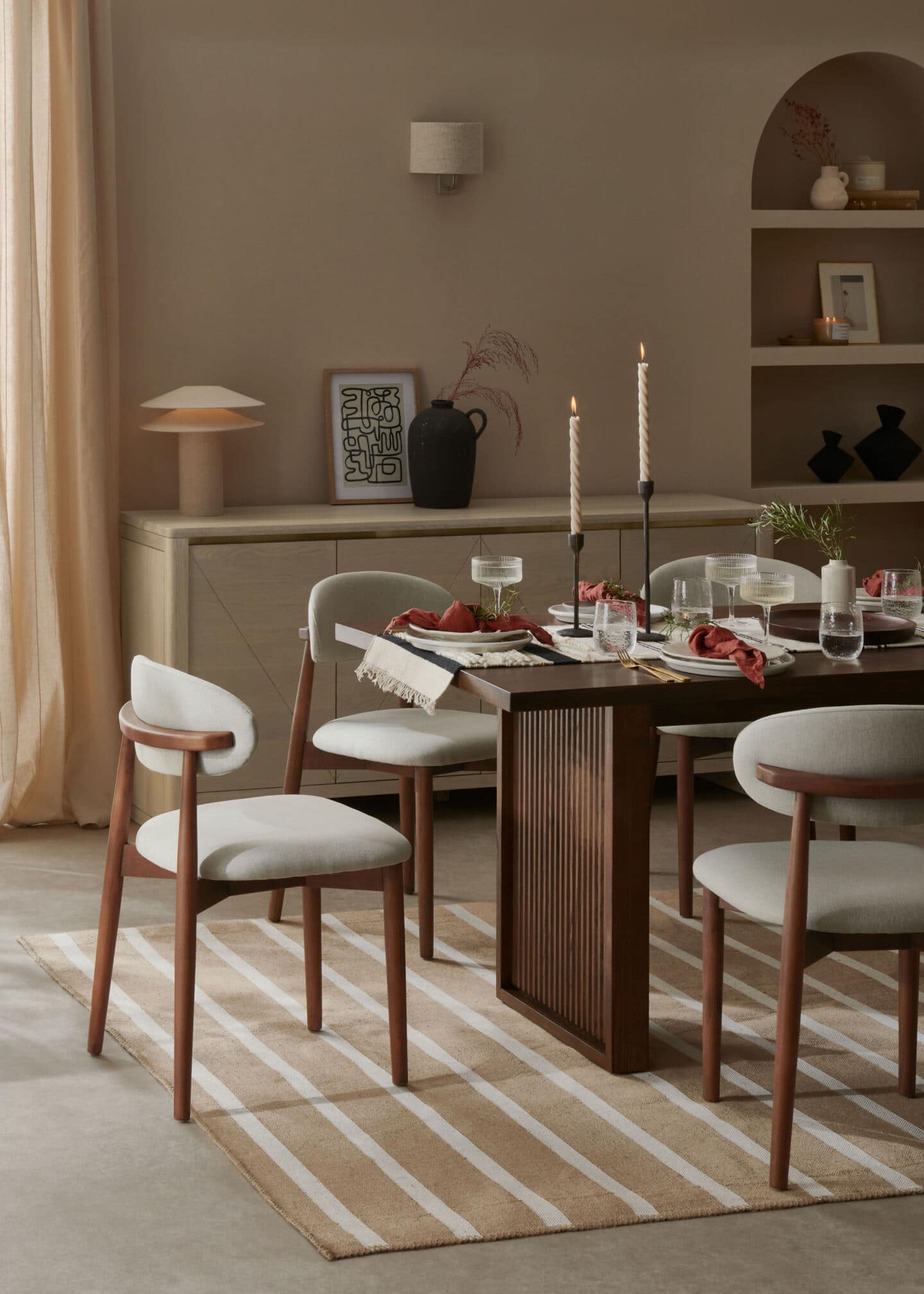 A Scandi style dining room in neutral colours. A light wood sideboard is behind a dark wood dining table. there are six upholstered wooden dining chairs