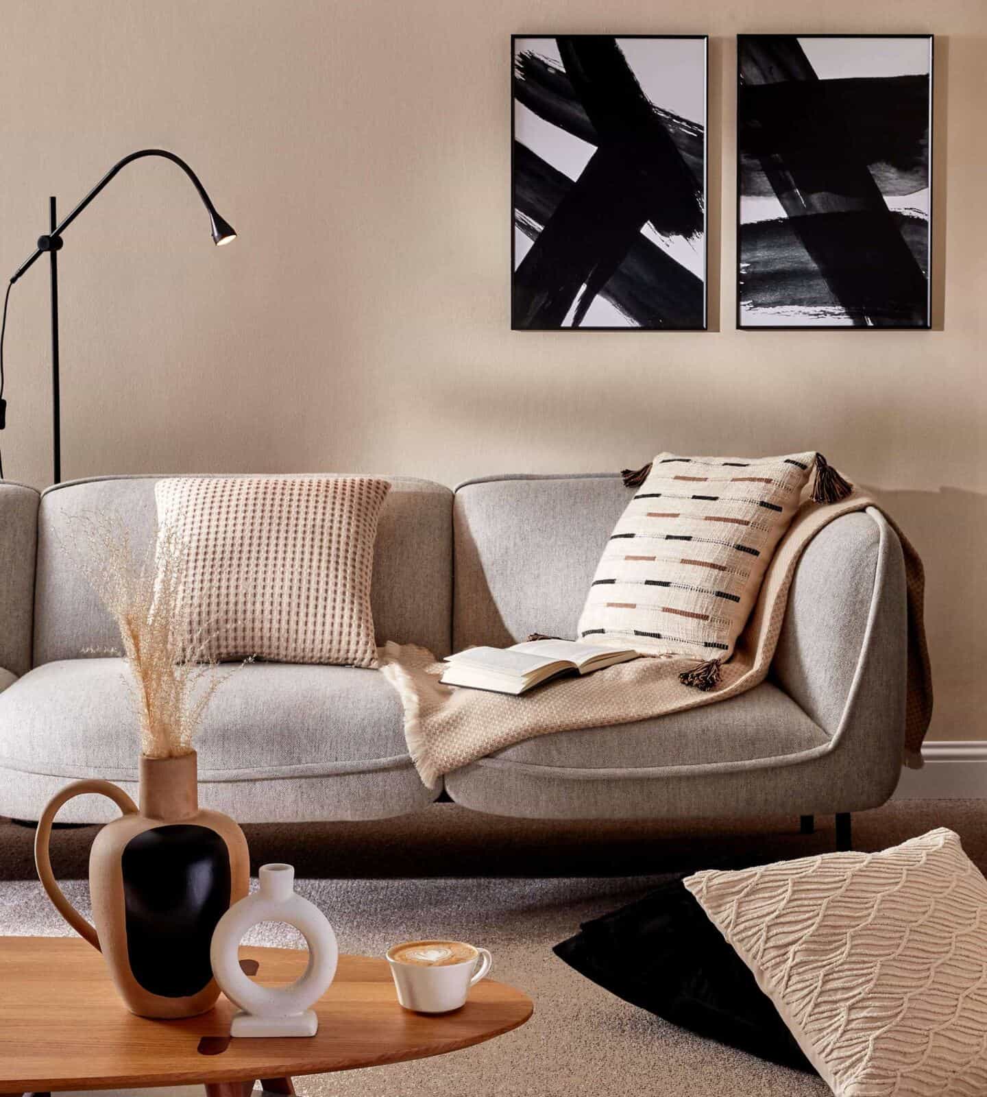 A coffee table in front of a grey sofa. Cushions and a blanket from the Primark Homeware range for SS22 are on the sofa and a selection of decorative accessories are on the table
