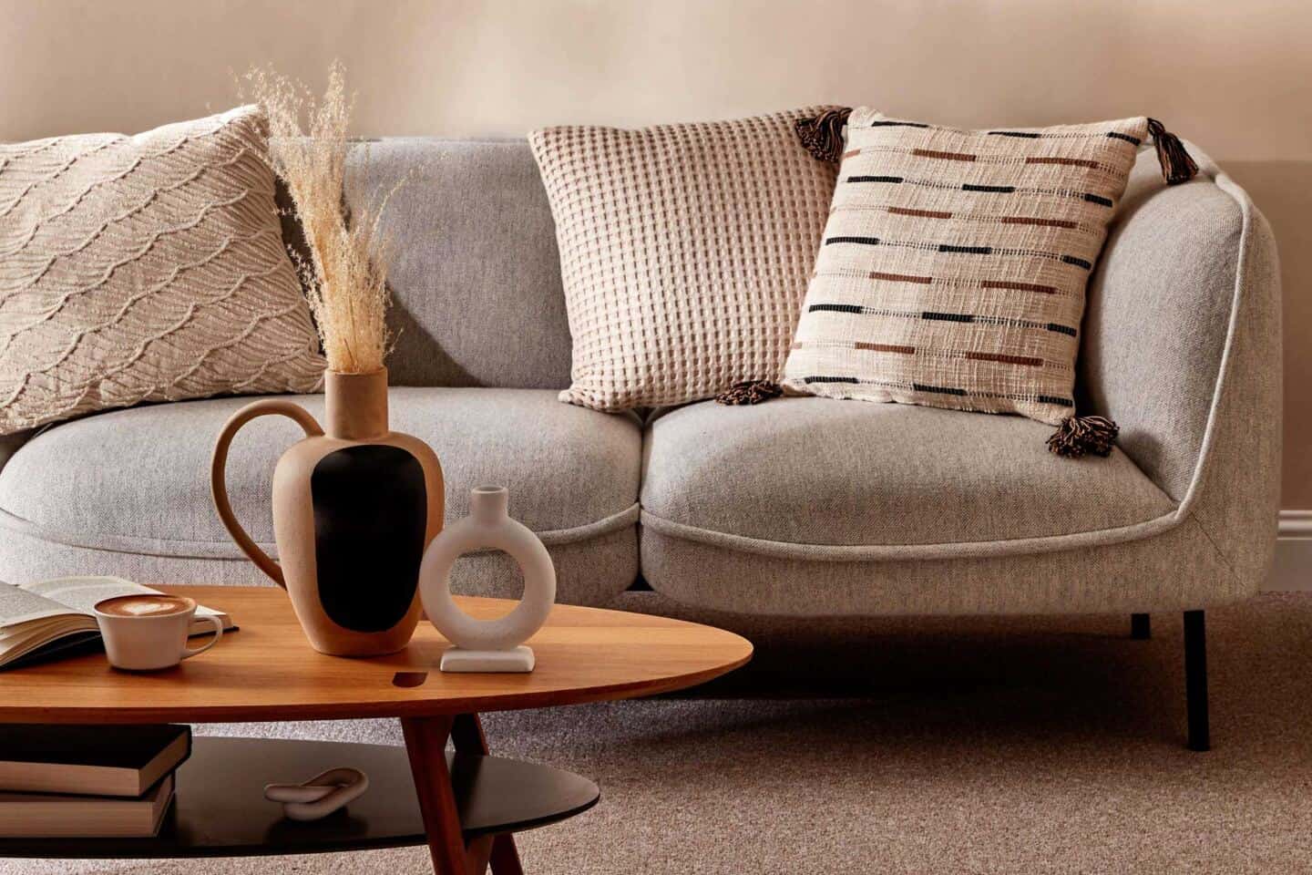 A coffee table in front of a grey sofa. Cushions from the Primark Homeware range for SS22 are on the sofa and a selection of decorative accessories are on the table
