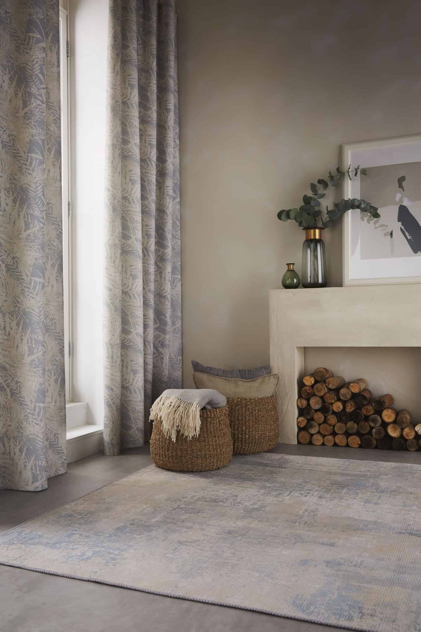 Textured Lives. Using texture in interiors to bring your home to life. Curtains with a nature-inspired pattern on them hang in a doorway. Two baskets next to a fireplace full of throws blankets and cushions.