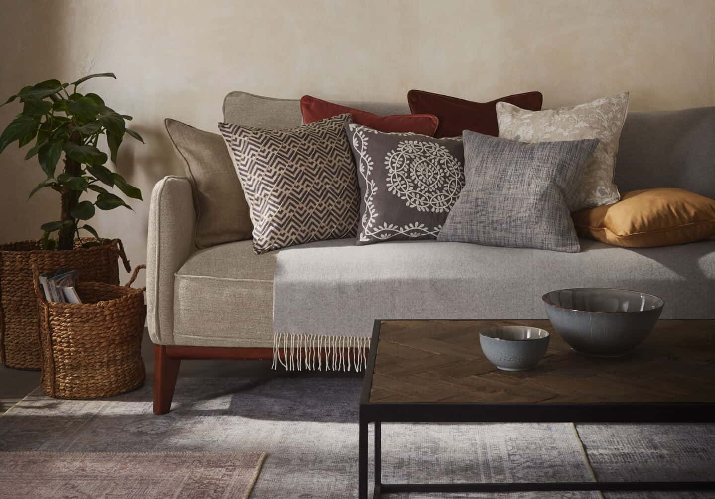 Textured Lives. Using texture in interiors to bring your home to life. A sofa is behind a coffee table whoch is on a rug. The sofa is covered in textured cushions in an earthy colour palette