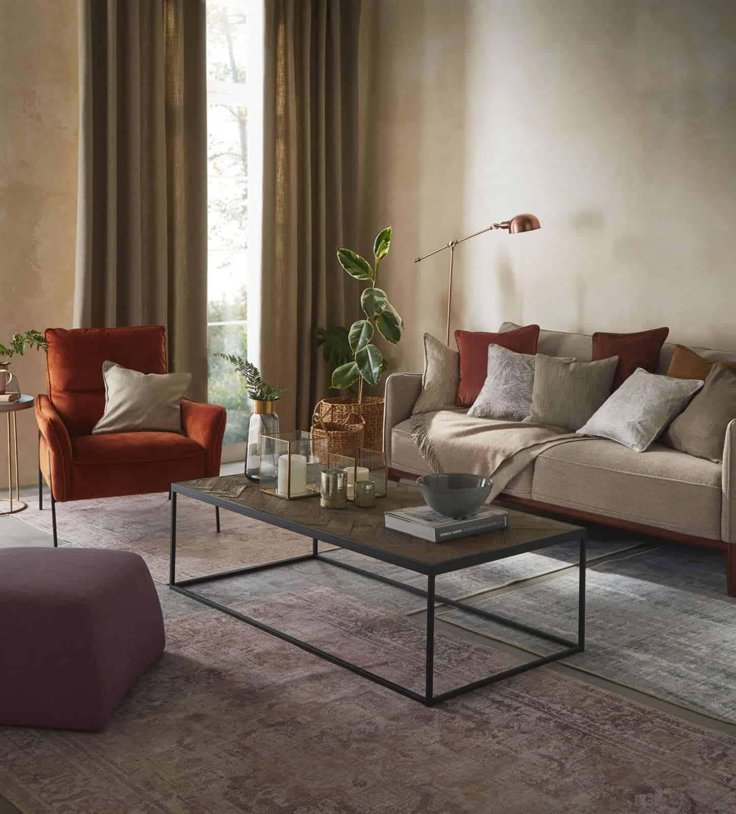 Textured Lives. Using texture in interiors to bring your home to life. A living room featuring sofa and armchair and pouffe around a coffetable on a rug. A window with curtains is behind the armchair.
