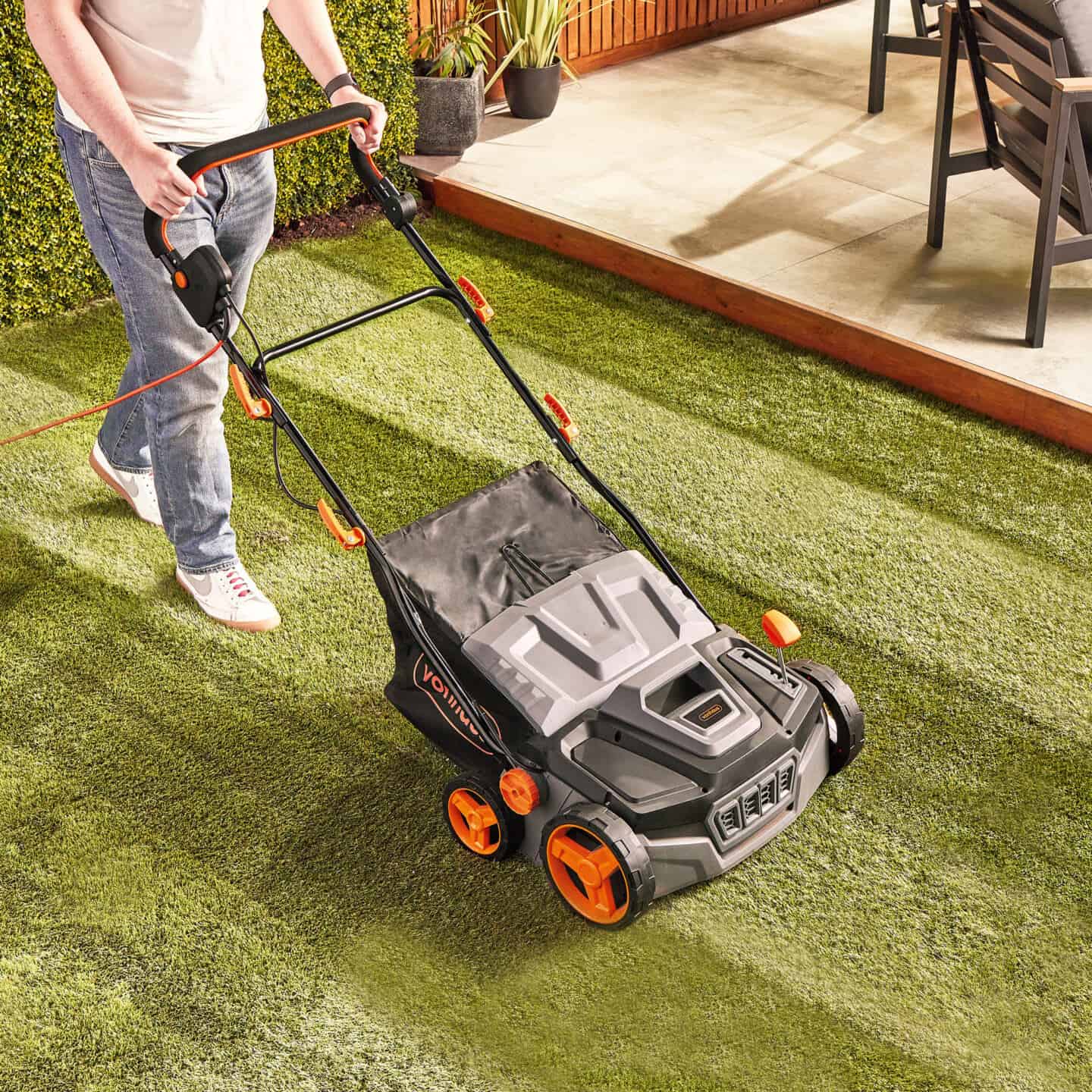 A man pushing an artificial grass brush across artificial grass. The brush looks just like a lawn mower